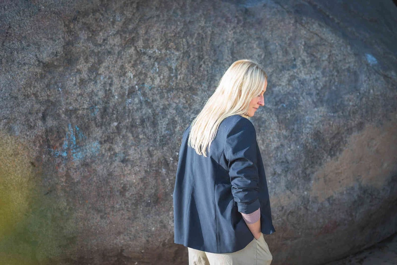 Frau steht vor einer Steinwand mit dem R&uuml;cken zur Kamera