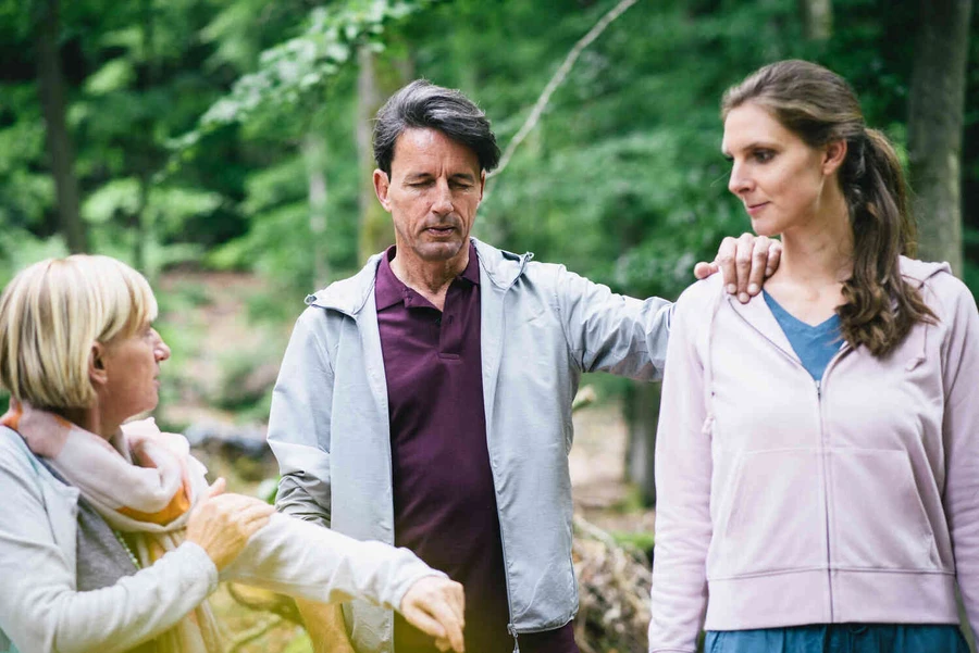 Mann steht mit geschlossenen augen drau&szlig;en mit zwei frauen und h&auml;lt sich an ihnen fest